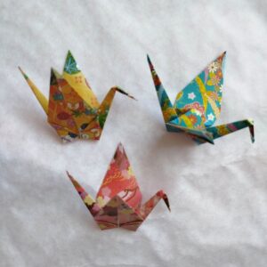 Three decorative origami cranes in yellow orange, pink red, and blue green made from Japanese chiyogami paper